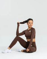 امرأة تجلس على الأرض مرتدية بلوزة نسائية قصيرة الأكمام بدون خياطة من BEST Power باللون البني الجوزي وبنطلون ضيق قصير.